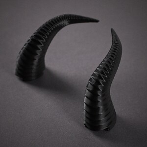 May include: A pair of black, textured, plastic horns. The horns are curved and have a pointed tip.