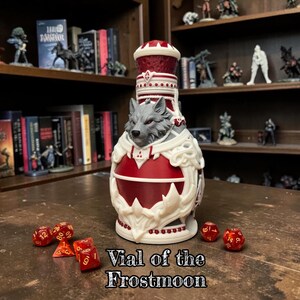 May include: A decorative container shaped like a potion bottle, featuring a sculpted grey wolf head at the center, accented with deep red and white details. The object is labeled Vial of the Frostmoon and is surrounded by several red polyhedral dice.