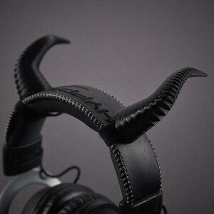 May include: Black leather headphones with a unique design featuring horns on the headband. The headphones have a stitched detail and a silver accent.