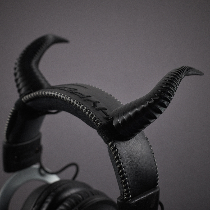 May include: Black leather headphones with a unique design featuring horns on the headband. The headphones have a stitched detail and a silver accent.