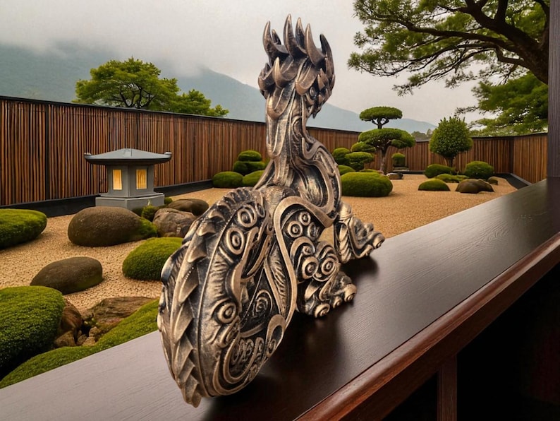 May include: Bronze-colored sculpture of a stylized creature with intricate details, resting on a dark wooden surface. The sculpture's design features patterns and textures. The background shows a Japanese garden with a stone lantern, gravel, and manicured shrubs.