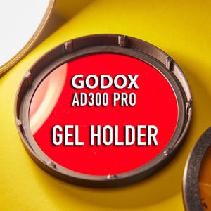 Op de afbeelding: Een rode gelhouder voor de Godox AD300 Pro flitser. De houder is gemaakt van zwart plastic en heeft een ronde vorm.