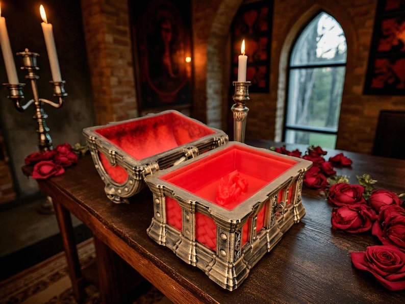 May include: An open, antique-style box with a red velvet interior sits on a wooden table, surrounded by red roses. The box has ornate metal detailing and a hinged lid. Lit candles and a candelabra are in the background.