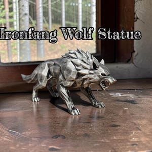 May include: A metallic gray wolf statue with the text "Ironfang Wolf Statue" above it. The wolf is in a snarling pose, with its mouth open, and is positioned on a wooden surface. The statue has a geometric design.