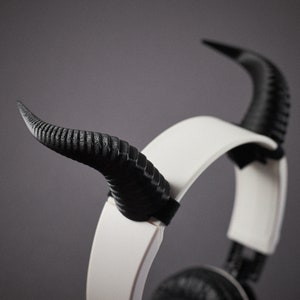May include: White headphones with black horns attached to the headband. The horns are made of a textured plastic.
