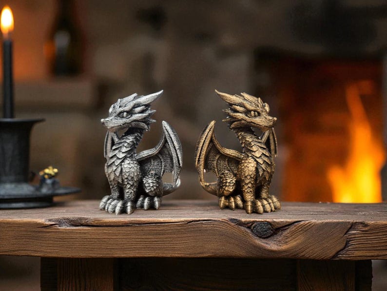 Puede incluir: Dos figuras detalladas de dragones, una plateada y otra dorada, se colocan una al lado de la otra sobre una superficie de madera. Los dragones tienen escamas intrincadas, alas y una expresi&oacute;n feroz. El fondo est&aacute; borroso, con una chimenea c&aacute;lida visible.