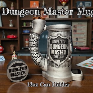 Könnte beinhalten: Ein silberfarbener Dungeon Master-Becher und Dosenhalter. Der Becher trägt den Text "BECAUSE I'M THE DUNGEON MASTER THAT'S WHY" auf einem Schild-Design. Der Dosenhalter trägt den Text "DUNGEON MASTER". Der Becher ist für eine 350ml Dose konzipiert.