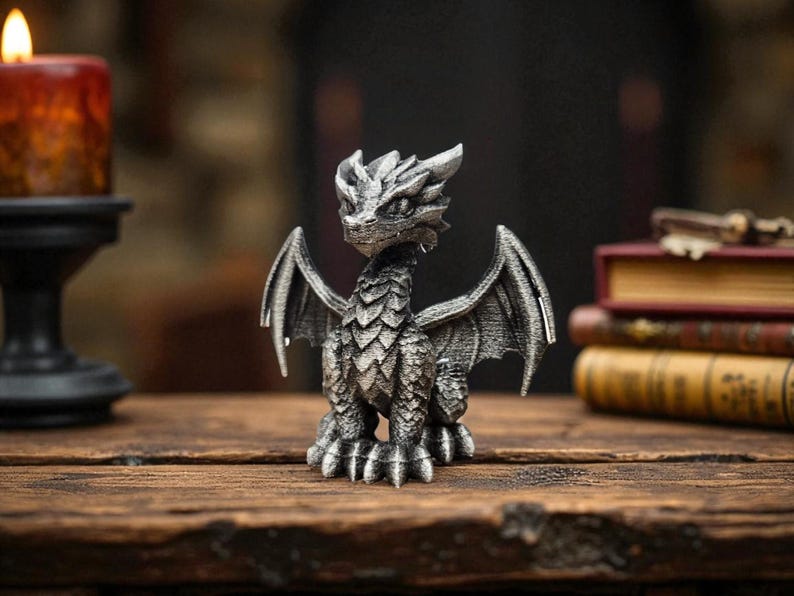 Puede incluir: Figura de drag&oacute;n plateado con escamas y alas detalladas. El drag&oacute;n est&aacute; posado sobre una superficie de madera, con una vela encendida y libros al fondo. La figura mide aproximadamente 13 cm de altura.