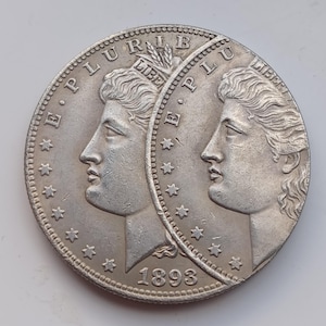 Peut inclure: Pièce de monnaie en argent représentant deux profils de femme, avec les inscriptions "E PLURIBUS UNUM" et "LIBERTY". L'année "1893" est visible. La pièce a un bord détaillé et des étoiles.