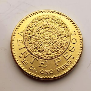 May include: A gold coin featuring a detailed Aztec calendar design in the center. The coin has the text "VEINTE PESOS" and "15 Gr. ORO PURO" around the edge. The coin has a ridged edge and a shiny finish.