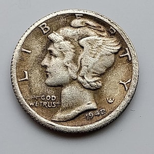 May include: A silver-coloured Mercury dime coin featuring a profile of Liberty wearing a winged cap facing left. The text LIBERTY is arched along the top, GOD WE TRUST is on the left, and the year 1942 is printed at the bottom right.