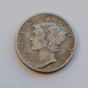Könnte beinhalten: Nahaufnahme einer silbernen Mercury-Dime von 1916. Sie zeigt das Profil einer Frau mit geflügelten Haaren, das Wort „LIBERTY“ und „IN GOD WE TRUST“. Die Münze weist Abnutzungserscheinungen auf.