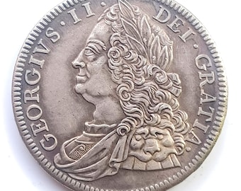 May include: A silver coin featuring a profile of a man with a laurel wreath and ornate clothing. The coin's edge has a textured pattern. The inscription "GEORGIVS II DEI GRATIA" is visible around the coin's edge.