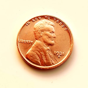 May include: A copper-colored 1931 penny with the profile of a man on the obverse. The coin features the inscriptions "IN GOD WE TRUST" and "LIBERTY". The year "1931" is visible. The coin is in good condition.
