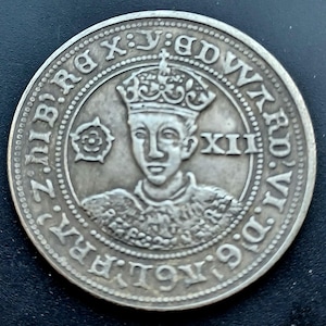 Puede incluir: Una moneda de plata con un retrato coronado y el número romano XII. La moneda tiene texto en el borde y un emblema floral. Esta moneda histórica es probablemente un objeto de colección.