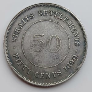May include: A silver Straits Settlements coin from 1890. The coin is inscribed with "STRAITS SETTLEMENTS" around the perimeter, and "FIFTY CENTS" along with the number "50" in the center. The coin has a detailed, textured surface.