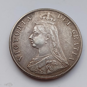 May include: A silver coin featuring a profile of a woman wearing a crown and a veil. The coin's edge has a beaded design, and the words "VICTORIA DEI GRATIA" are inscribed around the portrait. The coin is likely a collectible or historical item.