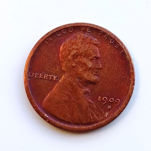 Puede incluir: Una moneda de centavo Lincoln de 1909 S de color cobre. La moneda presenta un perfil de Abraham Lincoln, la palabra "LIBERTY" y la inscripción "IN GOD WE TRUST". El año "1909" y la marca de ceca "S" también son visibles.