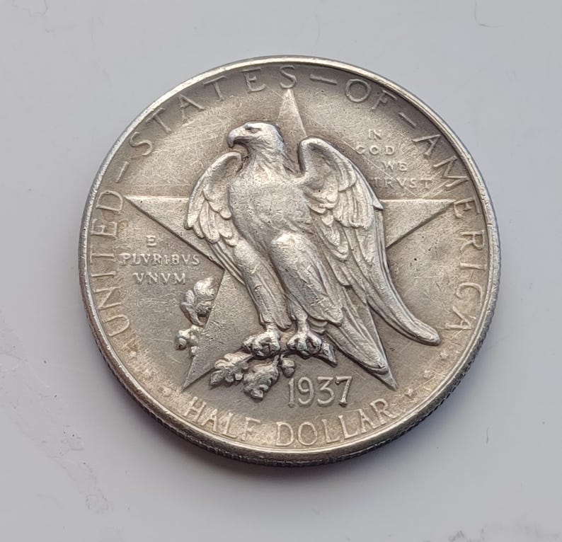 May include: A silver 1937 Half Dollar coin. The coin features an eagle perched on a star, with the words "UNITED STATES OF AMERICA" and "HALF DOLLAR" around the edge. The year 1937 is visible.