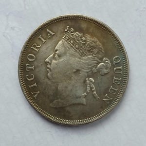 May include: A silver coin depicting Queen Victoria in profile, with the inscription "VICTORIA QUEEN" around the edge. The coin shows signs of wear, with a detailed border. A historical numismatic item.