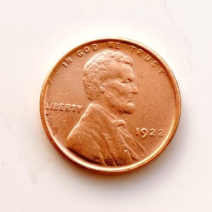 Peut inclure: Une pièce de monnaie Lincoln de 1922, de couleur cuivrée. L'avers présente un profil d'Abraham Lincoln, le mot "LIBERTY" et l'inscription "IN GOD WE TRUST". L'année "1922" est également visible.