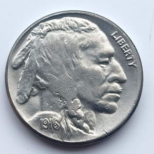 Könnte beinhalten: Eine silberne Münze mit dem Profil eines amerikanischen Ureinwohners, dem Wort "LIBERTY" und der Jahreszahl "1916". Die Münze weist ein detailliertes Design und ein leicht abgenutztes Aussehen auf.