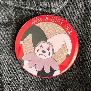Könnte beinhalten: Ein roter Ansteckknopf mit weißem Rand. Der Knopf zeigt einen Comic-Jester mit einem rosa und schwarzen Kostüm, einem traurigen Gesichtsausdruck und Glitzer im Hintergrund. Der Text "Just A Little Guy" ist in Weiß um den Jester herum geschrieben.