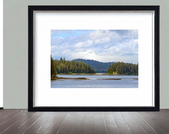 May include: A framed photograph of a scenic landscape with a body of water in the foreground and a forested hillside in the background. The sky is partly cloudy with a blue hue.