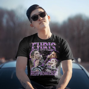 May include: Black t-shirt with a purple and white graphic print of Chris Motionless from the band Motionless in White. The graphic features a collage of images of Chris Motionless performing on stage.