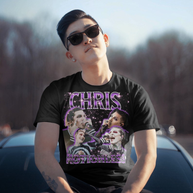 May include: Black t-shirt with a purple and white graphic print of Chris Motionless from the band Motionless in White. The graphic features a collage of images of Chris Motionless performing on stage.