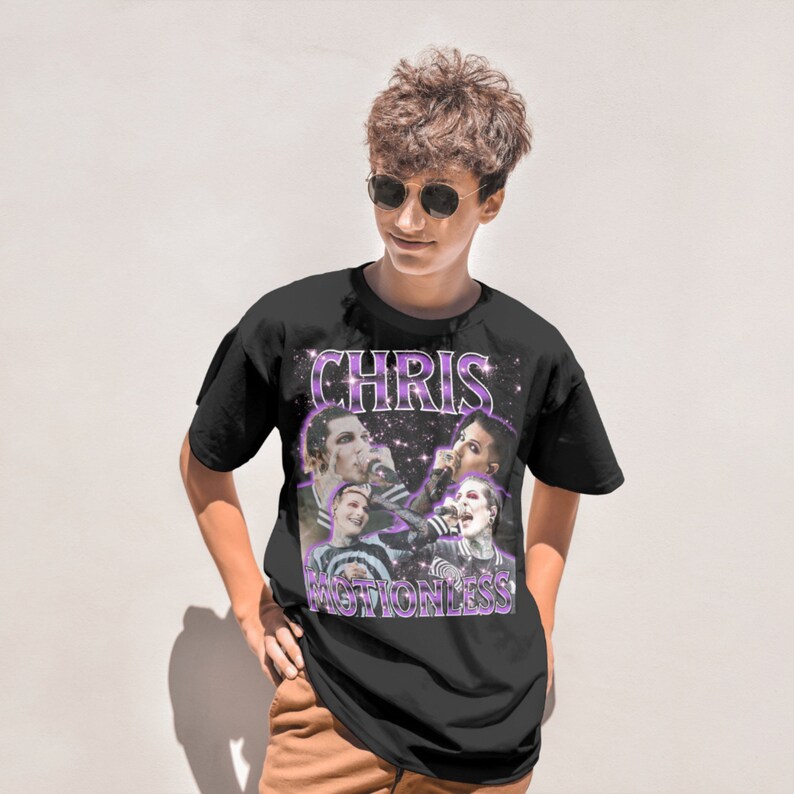 May include: Black t-shirt with a graphic print of Chris Motionless and the band Motionless in White. The graphic is in a retro style with a purple and white color scheme.