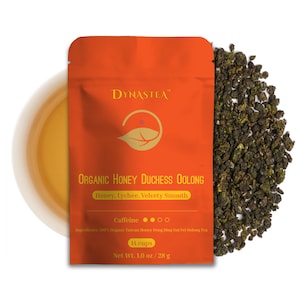 May include: An orange pouch of Dynastea Organic Honey Duchess Oolong tea with a leaf logo, next to a pile of loose tea leaves. The pouch text includes "Honey, Lychee, Velvety Smooth" and "14 cups, Net Wt. 1.0 oz / 28 g". A cup of tea is in the background.