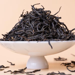 May include: A white ceramic bowl with a pedestal base filled with loose black tea leaves.