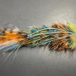 May include: A colorful fishing fly with a combination of feathers and synthetic materials. The fly features a mix of orange, blue, brown, and yellow hues, creating a vibrant and textured appearance. This fly is designed for attracting fish.