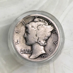 May include: A silver 1916 Mercury dime coin in a plastic coin holder. The coin features a profile of Liberty with the inscription "IN GOD WE TRUST" and the year "1916".