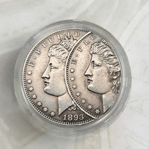 Può includere: Una moneta d'argento con due profili di donna che guardano a sinistra, circondati da stelle e dal testo "E. PLURIBUS UNUM" e "LIBERTY". La moneta ha anche il testo "E. PLURIBUS UNUM" e l'anno "1893".