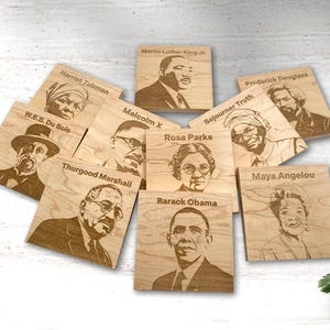 May include: Nine wooden coasters featuring engraved portraits of prominent African American figures, including Harriet Tubman, W.E.B. Du Bois, Martin Luther King Jr., Frederick Douglass, Sojourner Truth, Rosa Parks, Malcolm X, Thurgood Marshall, Maya Angelou, and Barack Obama.