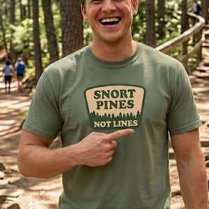 May include: Olive green t-shirt with the text "SNORT PINES NOT LINES" in a rectangular patch design. The shirt is a short-sleeved crew neck style. The word "Moss" is in the bottom right corner.