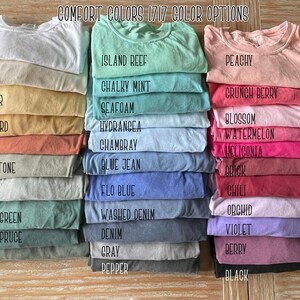 May include: Stacked folded t-shirts in various colors, including white, ivory, and butter. The image displays a range of options, with text labels identifying each color, such as "Island Reef," "Peachy," and "Black."
