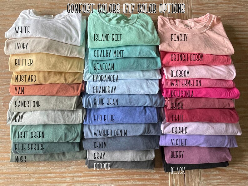May include: Stacked folded t-shirts in various colors, including white, ivory, and butter. The image displays a range of options, with text labels identifying each color, such as "Island Reef," "Peachy," and "Black."