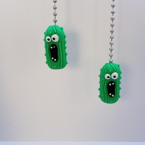 May include: Two green pickle-shaped light pull chains with white eyes and a black mouth. The pickles are hanging from silver chains.