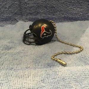 May include: A black football helmet with a red and white Houston Texans logo attached to a silver chain. The chain is used to pull a light switch.