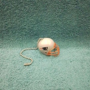 May include: A white and orange plastic football helmet with a Patriots logo. The helmet is attached to a silver chain.