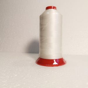May include: A spool of white thread with a red plastic base.