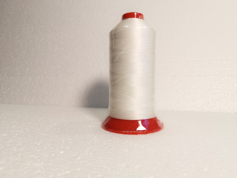 May include: A spool of white thread with a red plastic base.