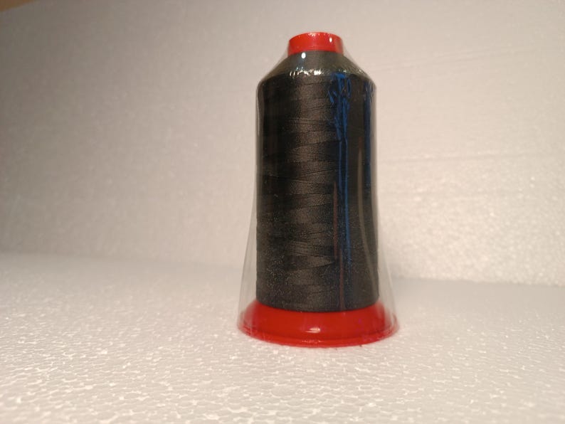 May include: A spool of black thread wrapped in clear plastic with a red plastic cap.
