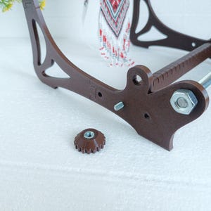 May include: A brown wooden bead loom with a metal rod and a silver nut. The loom is disassembled and the nut is lying on a white surface.