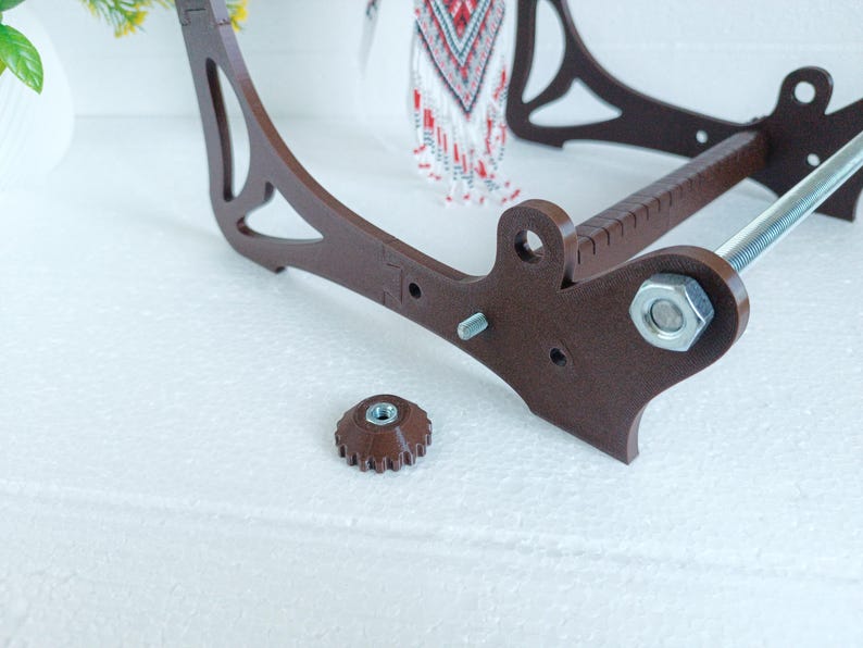 May include: A brown wooden bead loom with a metal rod and a silver nut. The loom is disassembled and the nut is lying on a white surface.
