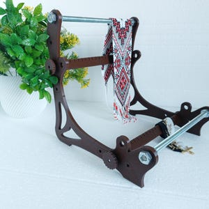 May include: A brown wooden stand with a metal rod and a beaded necklace hanging from it. The stand has a ruler on the side and is designed to hold jewelry.
