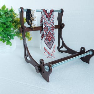 May include: A wooden stand with two beaded necklaces hanging from it. The stand has a metal rod across the top and a metal rod across the bottom. The stand is brown and the necklaces are white and red.